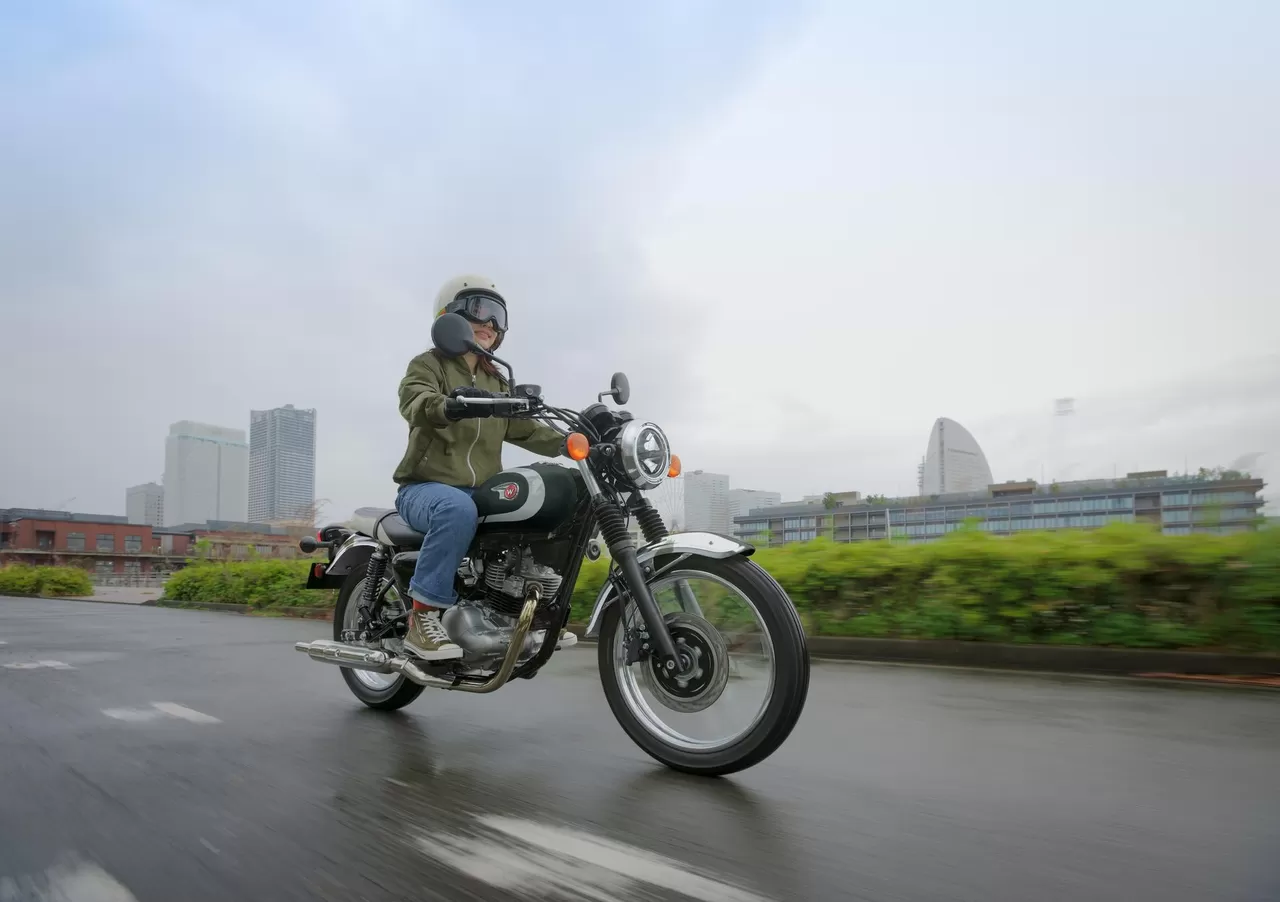 Rider on a green Kawasaki W230 beside a city waterfront